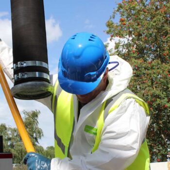 An AQS worker drops a pipe into a septic tank for cleaning